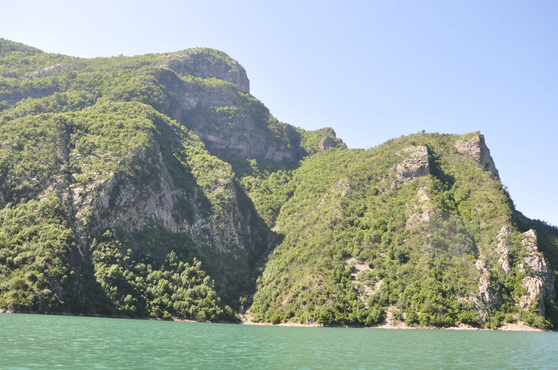 Mirror-like reflection of lush green mountains on the calm morning lake surface.