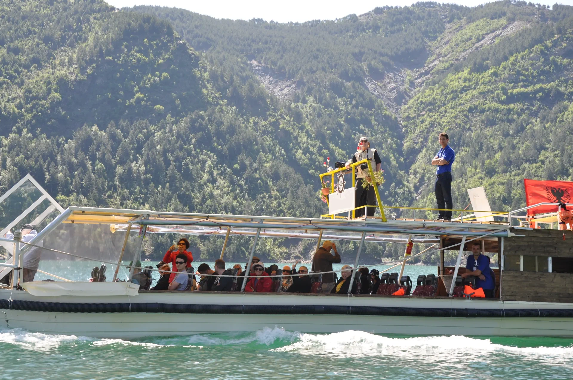 A tour boat filled with travelers enjoying the sunny cruise through the mountains.