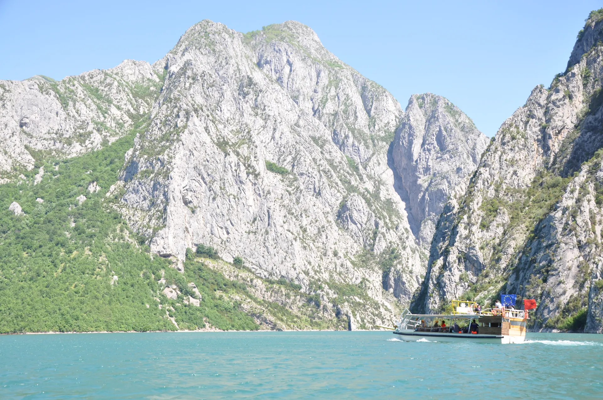 Tour boat passing beneath massive limestone overhangs on the winding Koman Lake route.