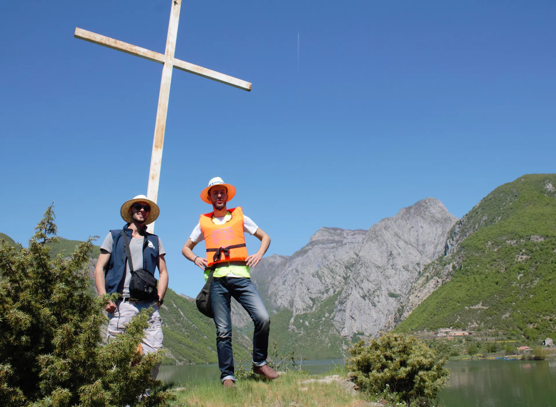 Travelers capturing memories at a scenic viewpoint marked by a cross overlooking the lake.