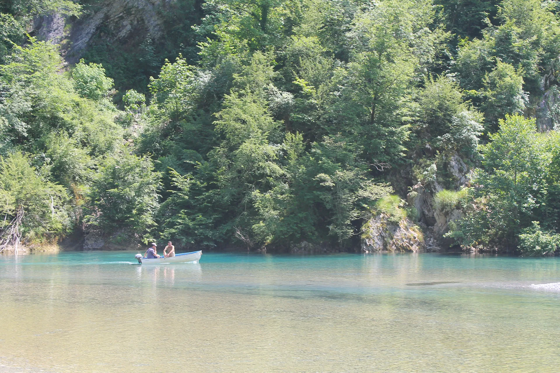 Small motorboat crossing the emerald expanse, dwarfed by massive surrounding peaks.
